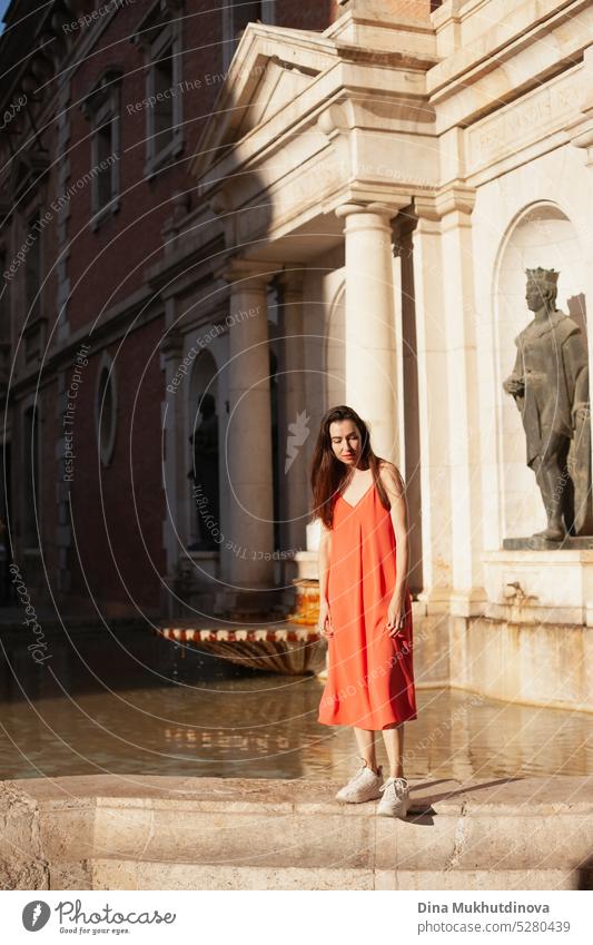 Junge Frau in rotem Kleid in der Nähe eines Brunnens. Weiblicher Tourist posiert für Fotoshooting. Mode und Stil. rotes Kleid Tourismus reisen im Freien jung