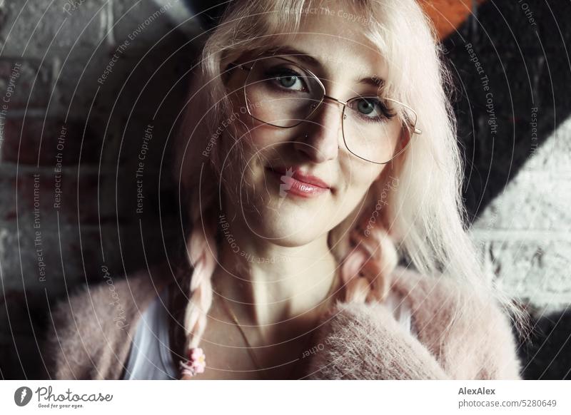 Junge Frau mit pink-blonden Haaren steht lächelnd vor einer Backsteinwand, die mit Graffiti verschandelt ist junge Frau Wand Portrait Brille schön schlank