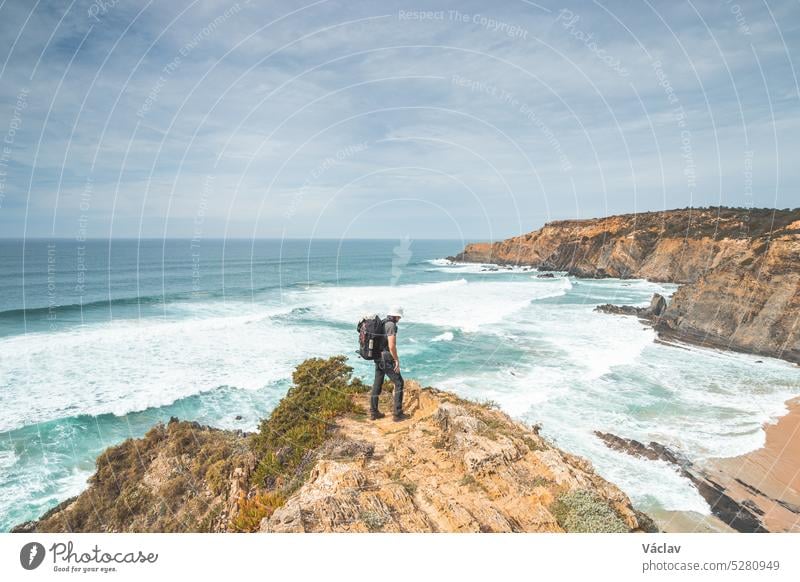 Wanderer und Abenteurer stehen an einer zerklüfteten Fels- und Steilküste und genießen den Blick auf den Atlantik im Westen Portugals in der berühmten Touristenregion Algarve