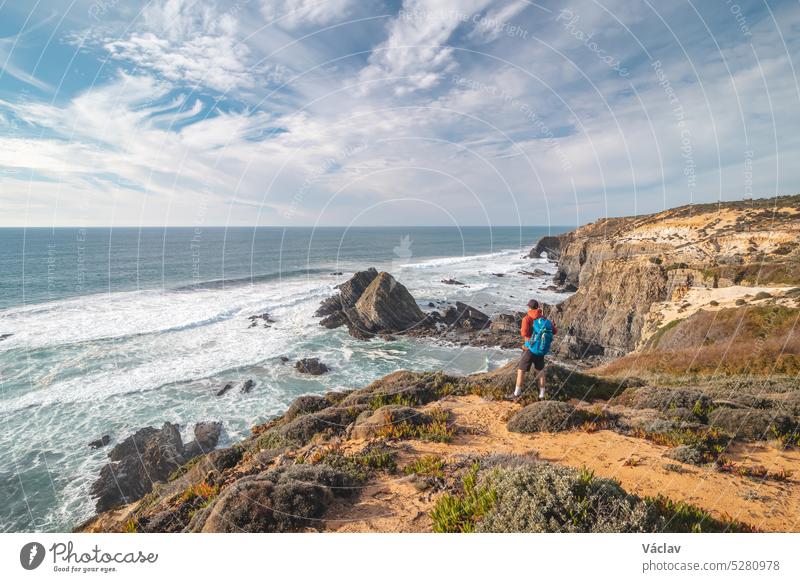 Freudiger Gesichtsausdruck eines jungen Rucksacktouristen, der am Rande einer Klippe mit Blick auf den Atlantischen Ozean in der Region Odemira im Westen Portugals steht. Wanderung entlang des Fisherman Trail, Rota Vicentina