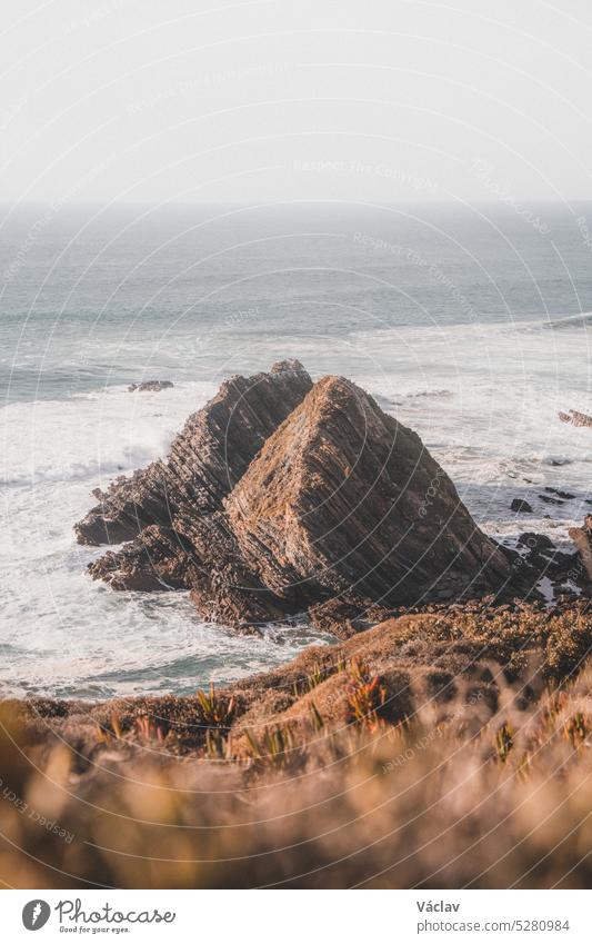 Futuristisch anmutende felsige Landzunge, die sich bei Sonnenuntergang aus dem Atlantik erhebt, in der Region Odemira, Westportugal. Wanderung entlang des Fischerpfads, Rota Vicentina