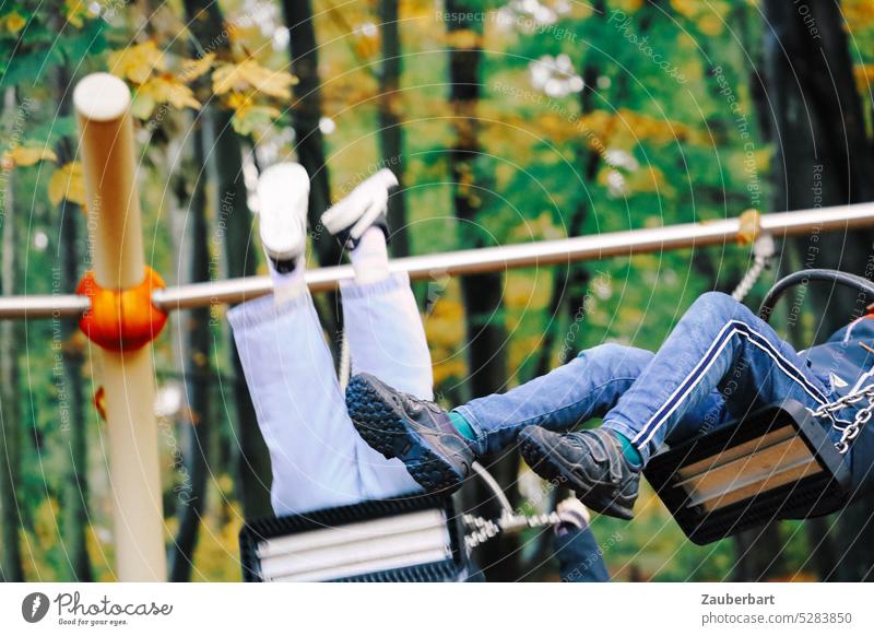 Beine von zwei Kindern in Bewegung auf der Schaukel vor Bäumen schaukeln spielen Spaß Kindheit Spielplatz ausgelassen toben Freude Lebensfreude Glück