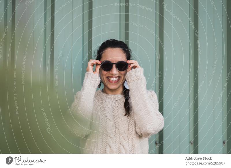 Fröhliche ethnische Frau mit Sonnenbrille Zaun Lächeln positiv Landschaft Natur Glück heiter sorgenfrei jung Metall lässig Freude Stil Optimist trendy Inhalt