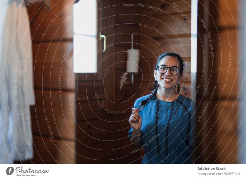 Frau mit Brille steht in der Tür Haus Lächeln Türöffnung positiv Bad heiter Kleid heimwärts jung Glück hölzern Stil Eingang Gebäude Lifestyle genießen Vergnügen