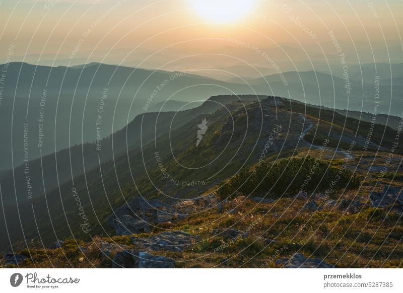 Sonnenaufgang in den Bergen. Natürliche Berglandschaft mit beleuchteten nebligen Gipfeln, nebligen Hängen und Tälern, blauer Himmel mit orange-gelbem Sonnenlicht