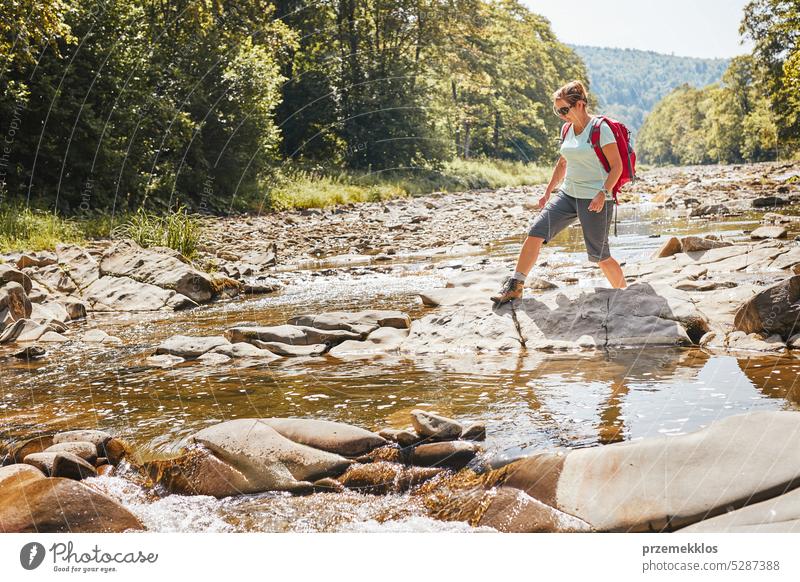 Trekking mit Rucksack Konzeptbild. Weibliche Backpacker trägt Trekking-Stiefel überqueren Berg Fluss. Frau Wandern in den Bergen während der Sommerreise