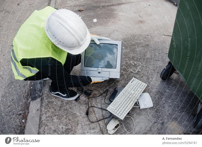 Ein Arbeiter in einem Recyclingzentrum sammelt einen alten Fernseher zwischen einer kaputten Tastatur und einer Computermaus. Technologie-Recycling-Konzept. Abfallwirtschaft