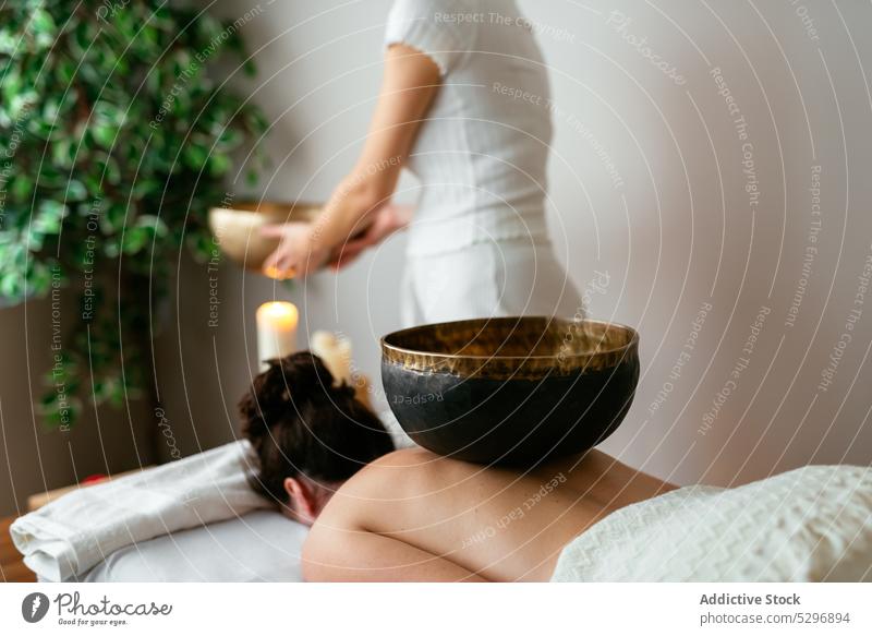 Anonyme Frau mit Klangschale an einem Schreibtisch mit Kerzen stehend meditieren Spa Salon Therapeut Tradition Sprit Zen Wellness Aroma Harmonie