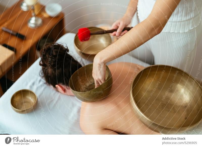 Eine Frau spielt eine Klangschale, die während der Meditation auf den Rücken einer Kundin gelegt wird. Frauen meditieren spielen Zen Musik Klient Erholung