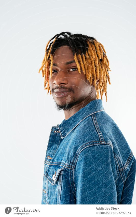 Stylischer schwarzer Mann mit Dreadlocks in Jeansjacke Stil Jeansstoff Outfit Lächeln Rastalocken Streetstyle cool Studioaufnahme Atelier selbstbewusst