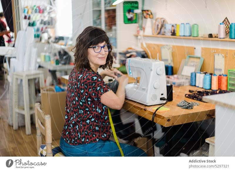 Zufriedene Frau an der Nähmaschine im Atelier Schneider Damenschneiderin Näherin nähen Lächeln Werkstatt professionell Handwerk Basteln kreativ Arbeitsplatz