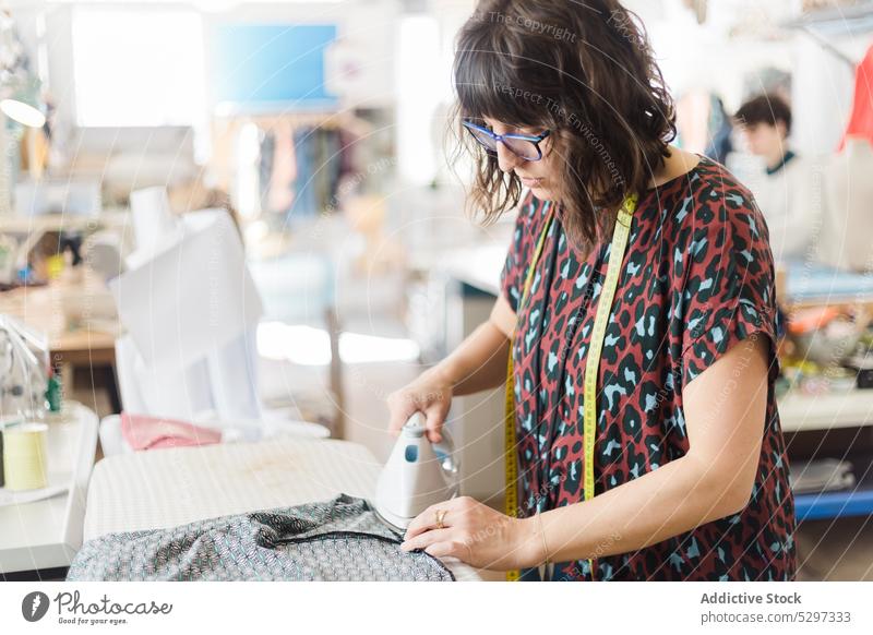 Frau bügelt Stoff im Atelier Damenschneiderin Klebeband messen bügeln Schneider Werkstatt professionell Arbeit Textil Gewebe Prozess Näherin Designer Job nähen