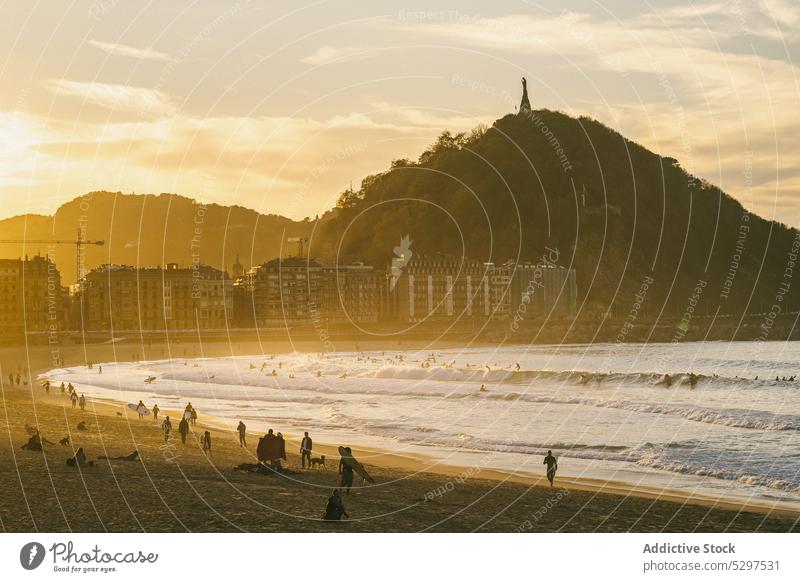 Touristen, die bei Sonnenuntergang am Meer spazieren gehen Menschen Strand MEER Resort Berge u. Gebirge Abend Gebäude Spaziergang winken Küste Ufer Wasser