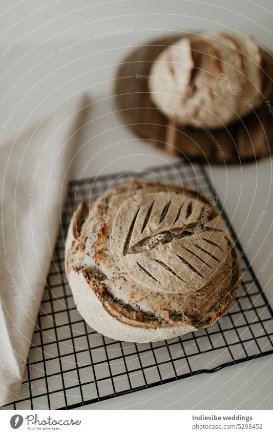 Selbstgebackenes Sauerteigbrot. Es ruht auf einem Kühlregal und einem Holzbrett. Auf der linken Seite befindet sich eine Leinenserviette. Minimalismus in einem vertikalen Flat-Lay-Bild.