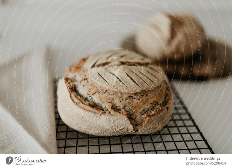 Selbstgebackenes Sauerteigbrot. Es ruht auf einem Kühlregal und einem Holzbrett. Auf der linken Seite befindet sich eine Leinenserviette. Brot Brotlaib