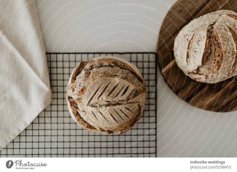 Selbstgebackenes Sauerteigbrot. Es ruht auf einem Kühlregal und einem Holzbrett. Auf der linken Seite befindet sich eine Leinenserviette. Minimalismus in einem horizontalen, flachgelegten Bild.