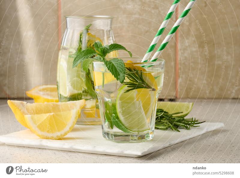 Limonade in einem transparenten Glas mit Zitrone, Limette, Rosmarinzweigen und Minzblättern auf weißem Hintergrund Kalk trinken Cocktail Erfrischung Frucht Eis