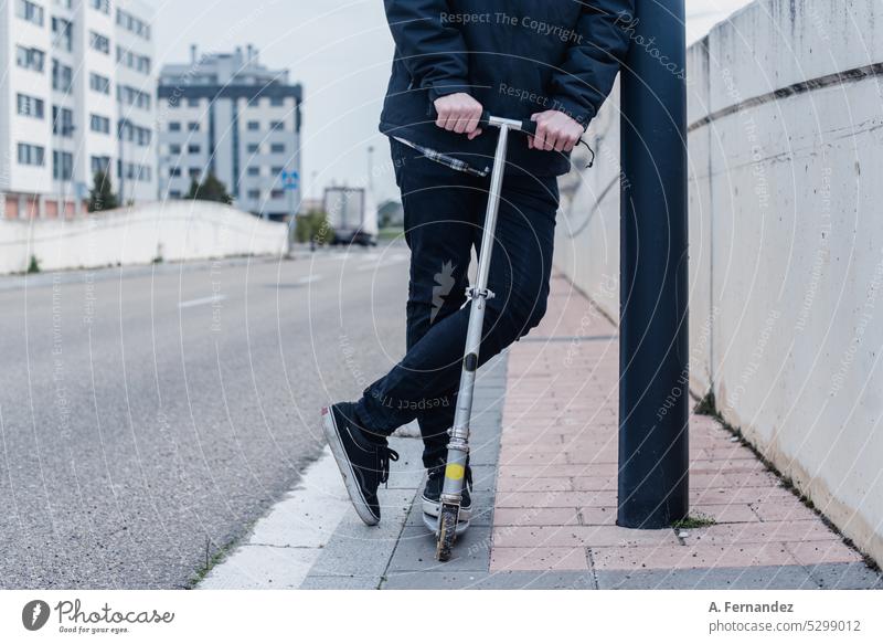 Junger Mann mit einem Kick-Scooter am Straßenrand. Konzept der ökologischen Transport Tretroller Kickroller urban elektrisch Mitfahrgelegenheit Lifestyle modern