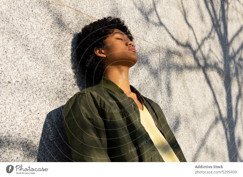 Ernster junger asiatischer Mann mit geschlossenen Augen im Sonnenlicht selbstbewusst cool Schatten Porträt gelb Vorschein Afro-Look Wand Stil ethnisch Frisur