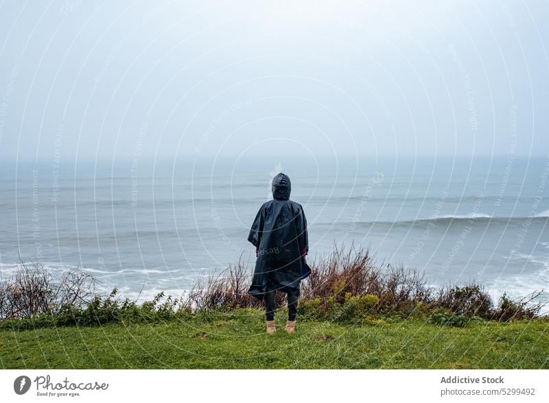 Anonymer Wanderer im Regenmantel bewundert die Meereslandschaft Frau Reisender winken Tourist MEER bewundern Natur Wanderung Unwetter stürmisch Himmel Wetter