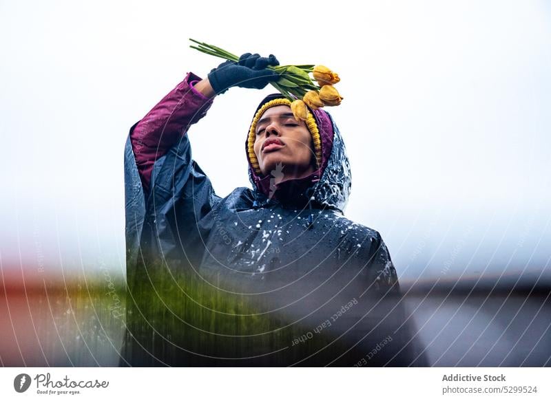 Schwarze Frau im Regenmantel mit Blumenstrauß Tulpe Augen geschlossen schäumen friedlich nachdenken ernst Natur Himmel Frühling Freiheit Windstille ruhig gelb