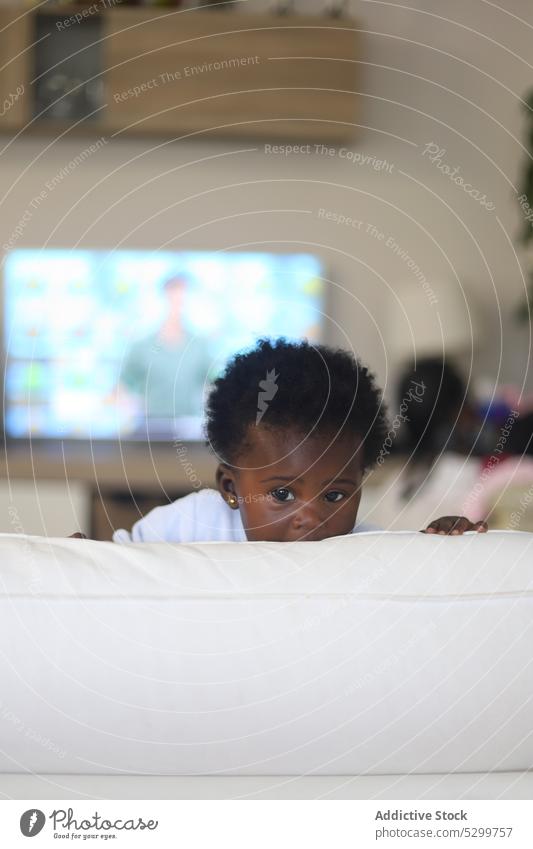 Niedliches schwarzes Kind versteckt sich hinter Kissen Baby Tierhaut Kopfkissen Wohnzimmer spielen heimwärts bezaubernd Kindheit niedlich schauen Sie wenig