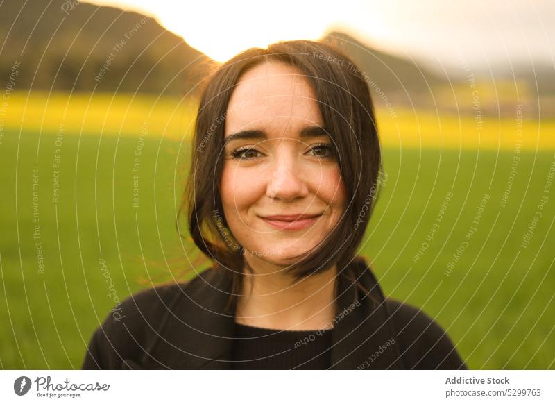 Lächelnde Frau auf grüner Wiese positiv Rasen Sonnenuntergang Landschaft Natur Himmel Abend Glück Freude jung Feld heiter Mantel Inhalt sorgenfrei Saison Gras