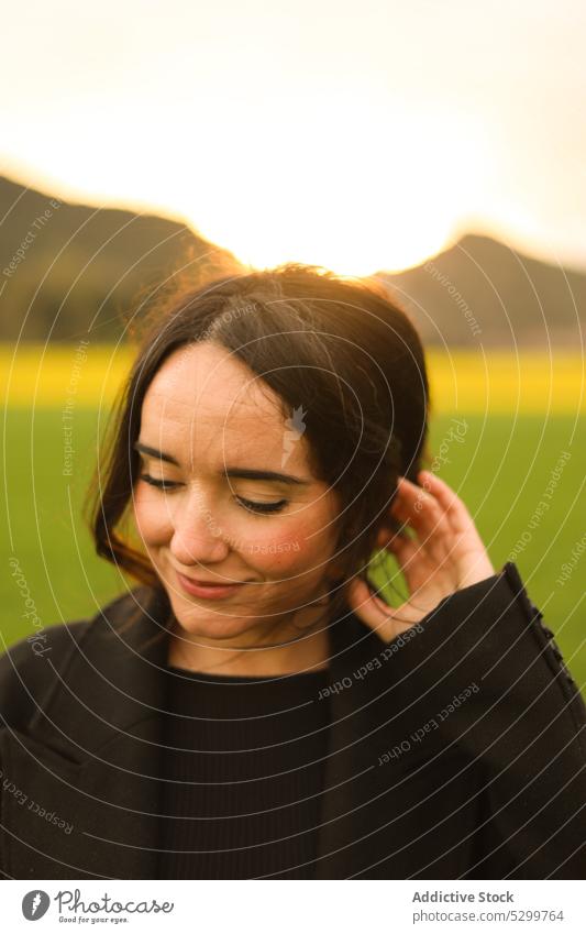 Lächelnde Frau auf grüner Wiese positiv Rasen Sonnenuntergang Landschaft Natur Himmel Abend Glück Freude jung Feld heiter Mantel Inhalt sorgenfrei Saison Gras