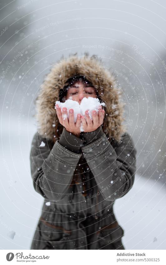 Zufriedene Frau, die Schnee aus den Händen bläst Winter Schneefall Schlag kalt Wald Natur Oberbekleidung Augen geschlossen Wetter Schneeflocke Wälder Frost