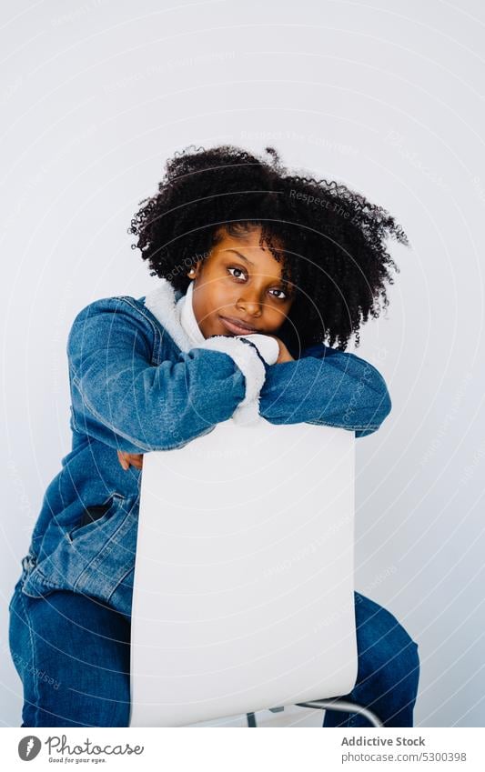 Charmante schwarze Frau lehnt sich an einen Stuhl Windstille Stil besinnlich Vorschein Jeanshose Mode trendy ernst nachdenklich afroamerikanische Frau Frisur