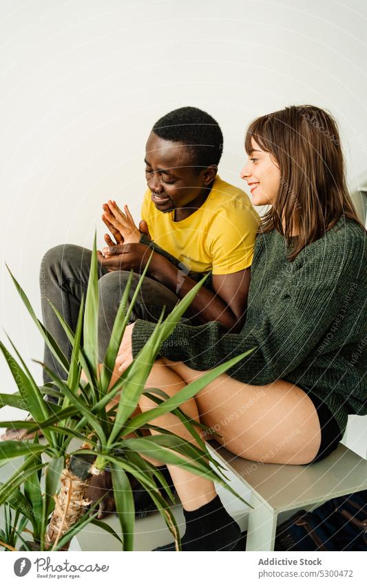 Lächelndes multiethnisches Paar hält sich an den Händen heiter Händchenhalten Partnerschaft Liebe Glück Zusammensein romantisch Treppe Pflanze lässig jung