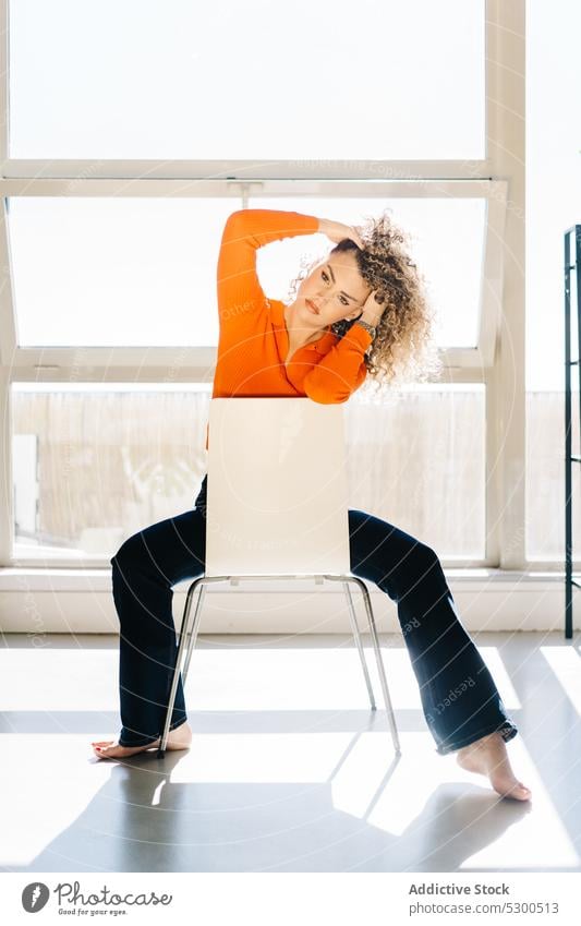 Unbekümmerte Frau berührt Haare auf einem Stuhl Haare berühren selbstbewusst ruhen Barfuß Stil Atelier Vorschein trendy Fenster lässig Windstille jung