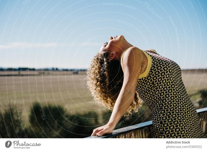 Unbekümmerte Frau lehnt den Kopf auf dem Balkon zurück sich zurücklehnen Freiheit Natur Feld Blauer Himmel Sonnenlicht Sommerzeit Landschaft jung Kleid