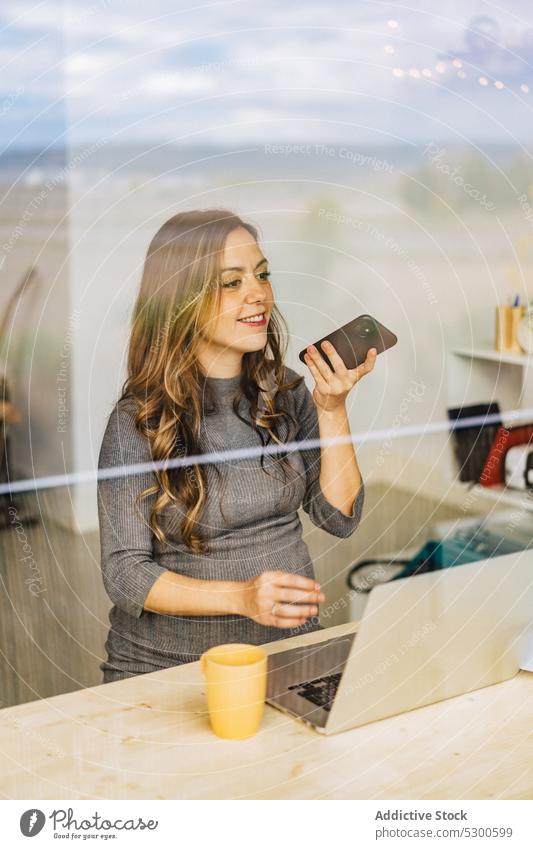 Fröhliche schwangere Frau, die eine Sprachnachricht aufnimmt, während sie am Laptop arbeitet benutzend Smartphone Aufzeichnen Stimme Nachricht Arbeit zu Hause