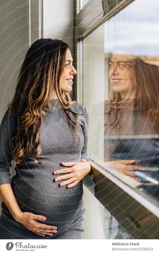 Schwangere Frau steht am Fenster und streichelt ihren Bauch schwanger Liebe Streicheln Bauch anfassen Mutterschaftsurlaub vorwegnehmen ruhig warten Lächeln jung