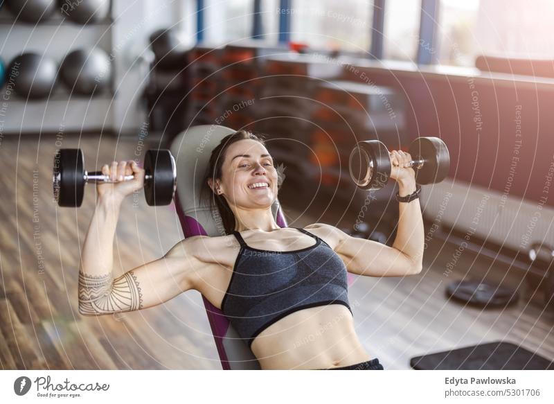 Junge Frau beim Training mit Hanteln in einem Fitnessstudio Wellness Wohlbefinden Bodybuilder sportlich Heben Bizeps Muskeln Curl-Hantel Bodybuilding Menschen