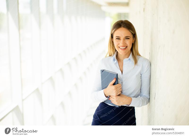 Junge Geschäftsfrau mit Notizbuch im Büroflur Frau professionell modern Notebook Flur jung Lächeln Business Arbeit Dame Gang positiv Karriere Kaukasier schön