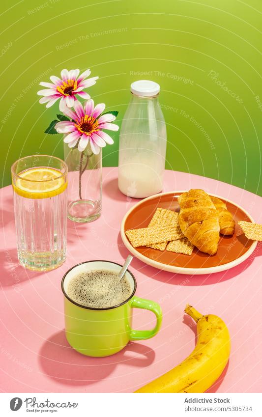 Leckeres Frühstück auf rosa Tisch Banane Blume Croissant Getränk Kaffee Wasser trinken melken Frucht Zitrone Vase frisch Tasse Flasche geschmackvoll lecker