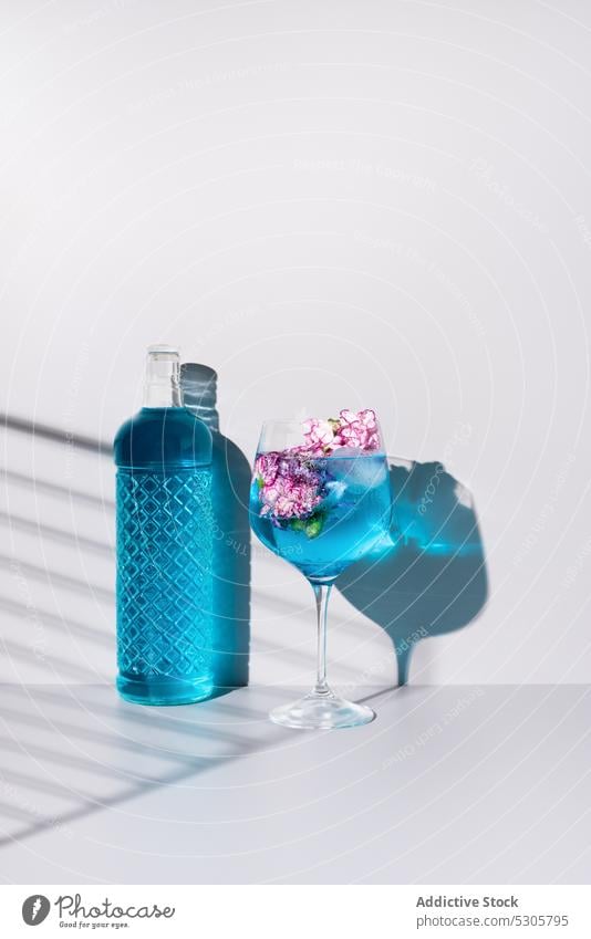 Erfrischender Cocktail mit Eiswürfeln bei Blumen und Flasche trinken Getränk blau Glas Alkohol Erfrischung kalt liquide Schatten Tisch Aperitif Blütezeit lecker