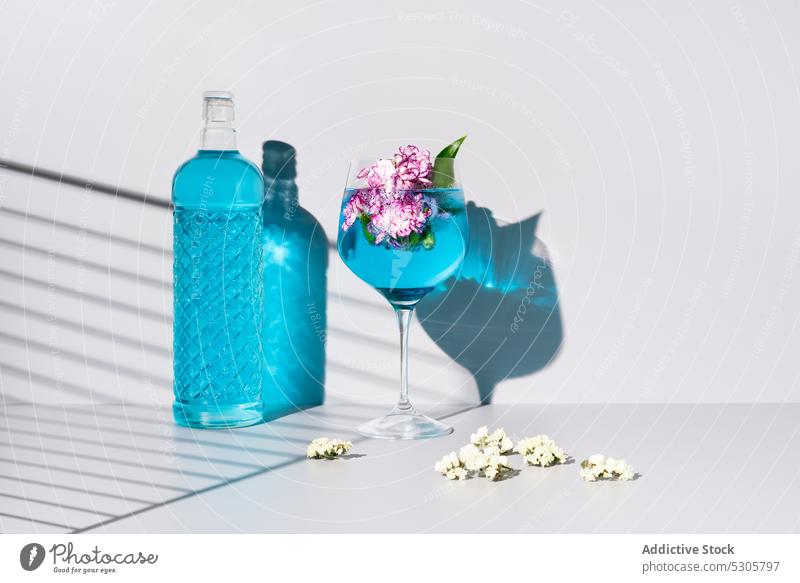 Erfrischender Cocktail mit Eiswürfeln bei Blumen und Flasche trinken Getränk blau Glas Alkohol Erfrischung kalt liquide Schatten Tisch Aperitif Blütezeit lecker