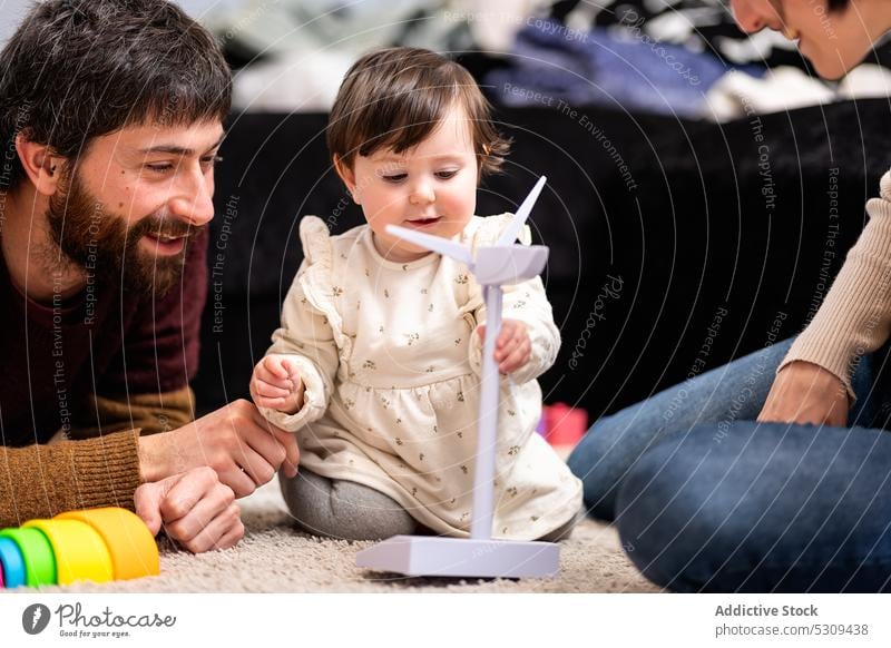 Glückliche Eltern mit ihrer Tochter, die mit einem Windrad spielt Familie Windmühle Turbine Spielzeug spielen heiter Zusammensein Bonden Liebe Mutter Vater