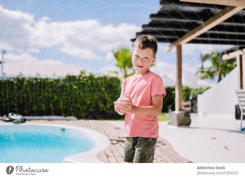 Niedlicher Junge mit Ballon im Hinterhof in der Nähe von Schwimmbad Sommer Luftballon Pool Resort Feiertag Sonne Kind Urlaub bezaubernd Kindheit niedlich Wasser