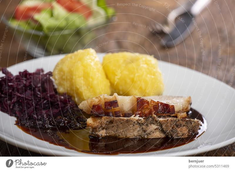 Bayerischer Schweinsbraten mit Knödeln Schweinebraten Soße Sauce Schweinefleisch Sonntagsbraten Braten bayerisch Bayern Brett rustikal Kraut Messer Gabel Gurke