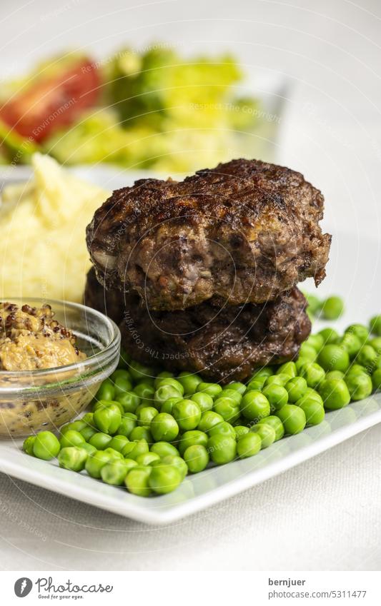 Bayerische Fleischpflanzerlmit Erbsen Hackbraten Bulette Hackfleisch gebraten Holz Hintergrund Gericht traditionell in Scheiben geschnitten Mahlzeit Essen