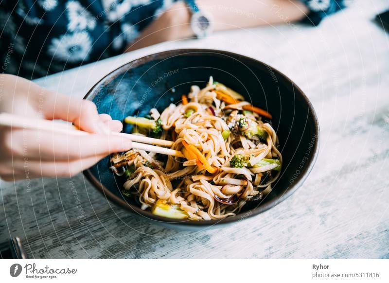 Frau isst asiatische Nudeln Udon mit Schweinefleisch im Cafe. Asiatische Nudeln Udon mit Schweinefleisch Nahaufnahme in einer Schüssel auf dem Tisch schwarz