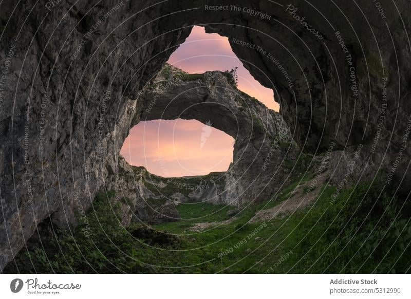 Doppellochhöhle in bergigem Gelände vor Sonnenuntergang Höhle Golfloch Berge u. Gebirge felsig Formation grün Gras farbenfroh malerisch Landschaft lebhaft Farbe