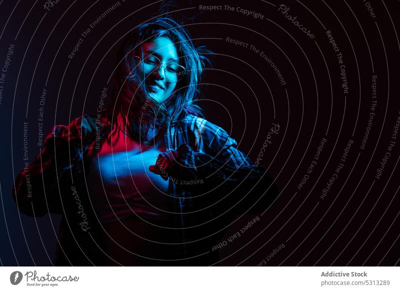 Fröhliche Frau mit Brille in der Dunkelheit mit Neon-Beleuchtung Glück Lächeln heiter Porträt positiv Stil neonfarbig genießen lässig jung Zahnfarbenes Lächeln