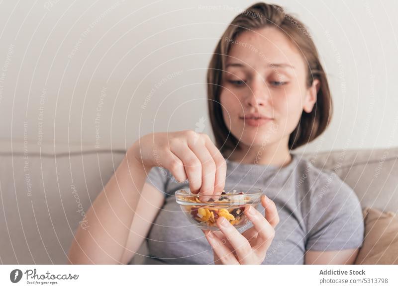 Charmante Frau isst leckeren Snack auf dem Sofa essen positiv Lächeln Gesundheit Komfort heimwärts Vergnügen Liege jung lässig Inhalt genießen Kurze Haare