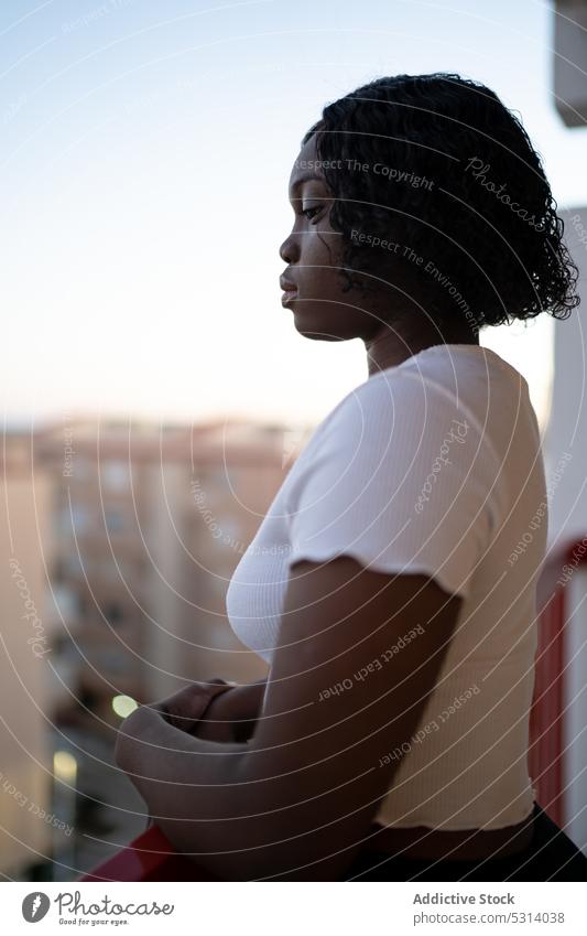 Schwarze Frau bewundert Stadtbild auf Balkon Terrasse bewundern Reling Gebäude Vorschein Großstadt urban krause Haare Straße ethnisch Windstille Top Afro-Look