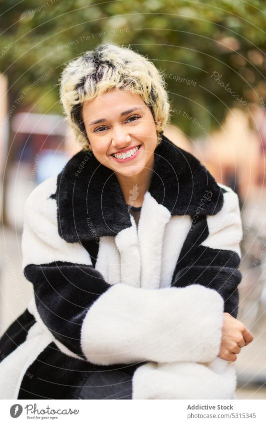 Ruhige junge Frau in modischem Mantel schaut in die Kamera Straße Fell Vorschein Stil trendy Großstadt Outfit Porträt urban charmant Bekleidung feminin